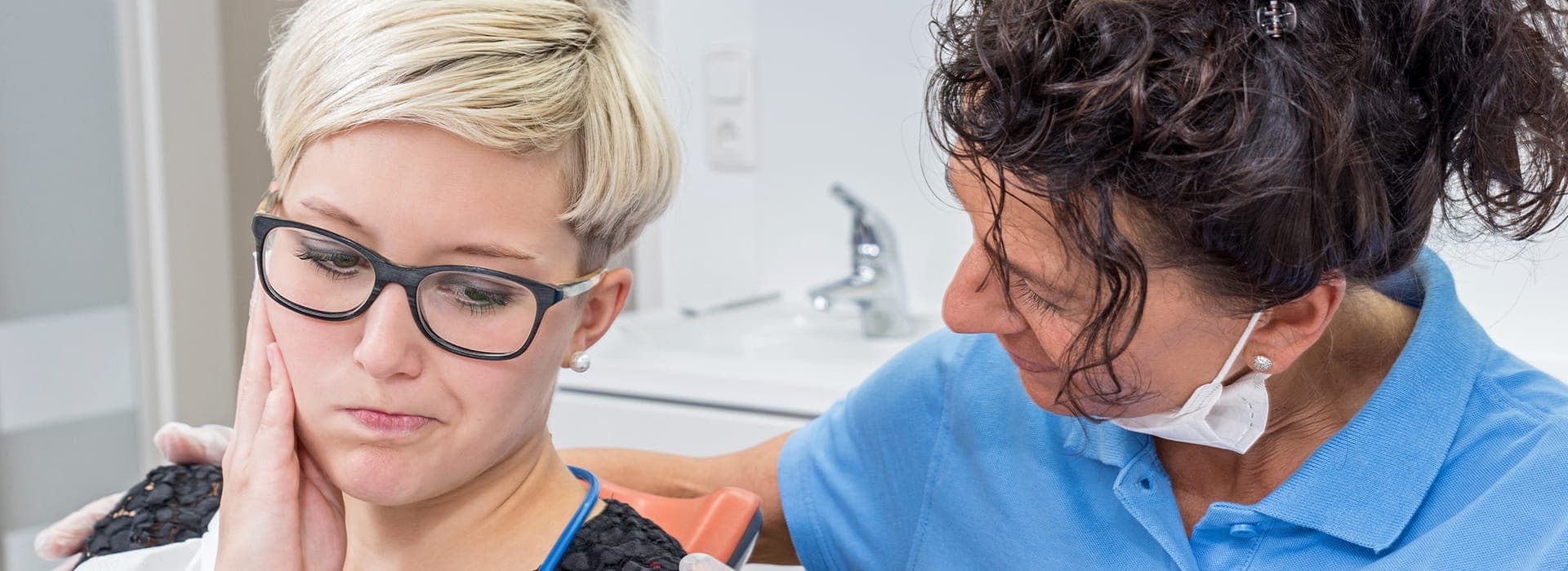 A patient holding her jaw in discomfort while a dental team member checks on her